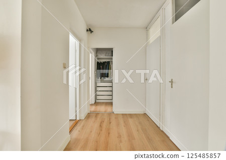 A minimalist hallway featuring white walls and wooden flooring, leading to a closet area, exemplifying modern interior design aesthetics. A minimalist hallway featuring white walls and wooden flooring, leading to a closet area, exemplifying modern interior design aesthetics. 125485857