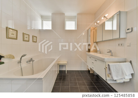 A sleek and contemporary bathroom featuring a bathtub, dual sinks, and stylish mirrors with natural light filtering through the windows, creating a serene ambiance. 125485858
