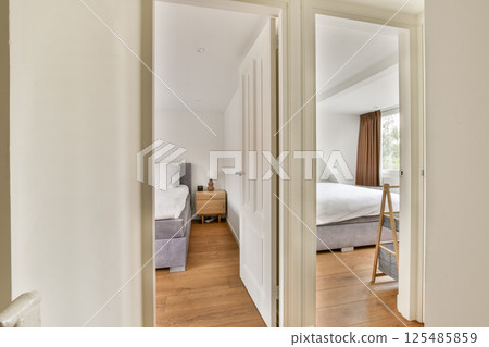 A glimpse into a modern, minimalistic bedroom featuring wooden flooring, neutral color tones, and natural light streaming in from a window. 125485859