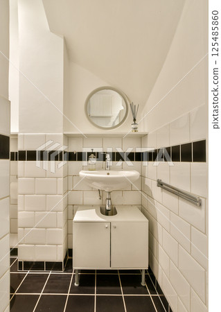 A contemporary bathroom showcasing clean lines and minimalist design, featuring a round mirror and elegant fixtures against a tiled wall. A contemporary bathroom showcasing clean lines and minimalist design, featuring a round mirror and elegant fixtures against a tiled wall. 125485860