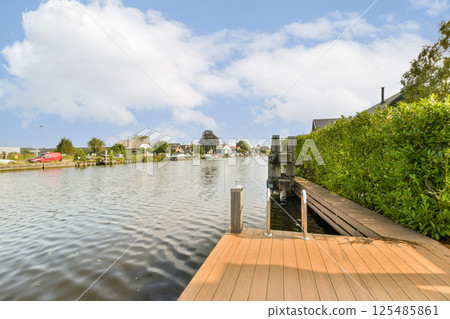 A peaceful view of a waterway lined with greenery and a wooden dock, showcasing a tranquil setting for relaxation and nature enjoyment. A peaceful view of a waterway lined with greenery and a wooden dock, showcasing a tranquil setting for relaxation and nature enjoyment. 125485861