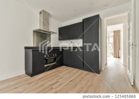 A sleek and modern kitchen featuring minimalistic design with dark cabinets, a shiny countertop, and a bright entrance leading to natural light. 125485868