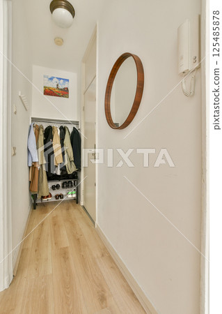 A stylish hallway featuring a mirror, coat rack, and wooden flooring. The space is well-lit and designed for functionality, showcasing an organized entryway. 125485878