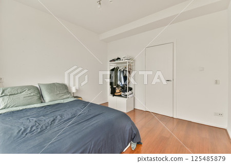 A modern minimalist bedroom featuring a neatly made bed with simple bedding, wooden floor, and minimalistic decor creating a serene atmosphere. 125485879
