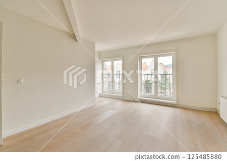 A bright and airy modern room showcasing large windows that offer a view of the outside. The wooden flooring adds warmth to the minimalist space. 125485880