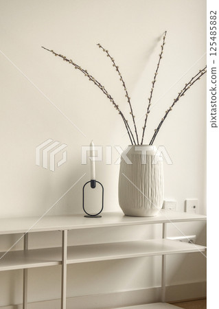 A minimalist interior setup featuring a large textured vase with branches and a chic candle holder on a sleek console table, showcasing modern design elements. 125485882