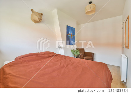A well-designed bedroom with minimalistic decor featuring a warm color scheme, a comfortable bed, and contemporary artwork on the wall. A well-designed bedroom with minimalistic decor featuring a warm color scheme, a comfortable bed, and contemporary artwork on the wall. 125485884