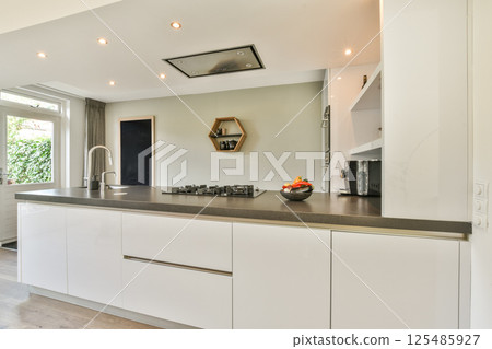 A contemporary kitchen featuring sleek cabinetry and a minimalist design, complemented by natural light and stylish fixtures. Ideal for modern home aesthetics. 125485927
