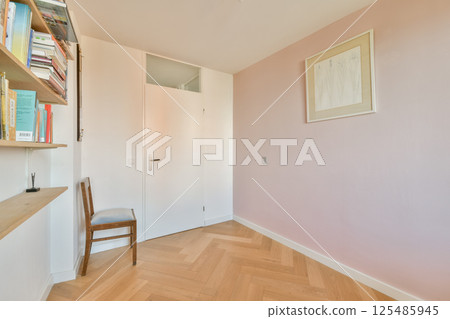 A serene interior space showcasing a minimalist design with wooden flooring, a simple chair, a colorful bookshelf, and soft wall hues. A serene interior space showcasing a minimalist design with wooden flooring, a simple chair, a colorful bookshelf, and soft wall hues. 125485945