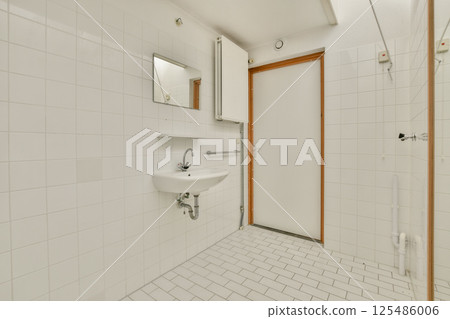 A spacious and airy bathroom featuring sleek white tiles, a modern sink, and a clean door design, epitomizing minimalist aesthetics and functionality. 125486006