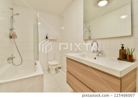 A sleek and contemporary bathroom featuring a bathtub, modern sink, large mirror, and minimalist decor. Ideal for showcasing stylish interior design. A sleek and contemporary bathroom featuring a bathtub, modern sink, large mirror, and minimalist decor. Ideal for showcasing stylish interior design. 125486007