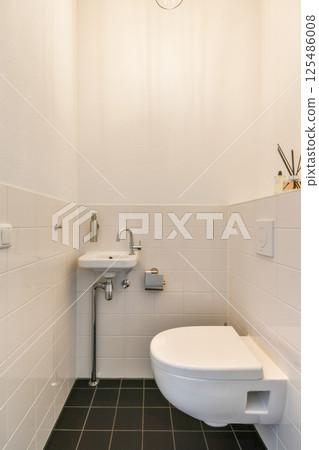 A clean and stylish modern bathroom featuring sleek white tiles, a minimalist sink, and a toilet, creating an uncluttered and serene space. A clean and stylish modern bathroom featuring sleek white tiles, a minimalist sink, and a toilet, creating an uncluttered and serene space. 125486008