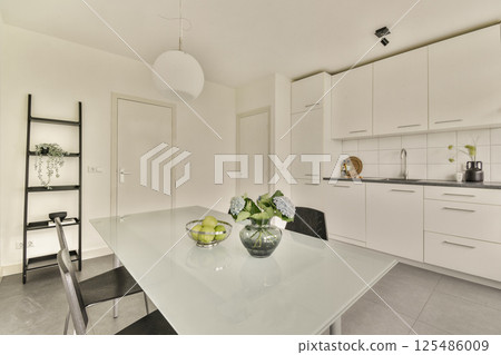A sleek and minimalistic kitchen with a dining table, elegant lighting, and a touch of greenery, showcasing contemporary interior design aesthetics. A sleek and minimalistic kitchen with a dining table, elegant lighting, and a touch of greenery, showcasing contemporary interior design aesthetics. 125486009