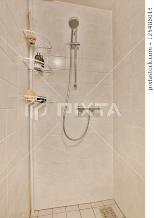 A minimalist shower stall featuring clean tile walls and a sleek design with a showerhead and shelving for toiletries, perfect for contemporary bathrooms. 125486013