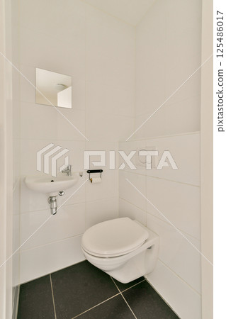 A sleek and modern bathroom featuring white tiled walls, a minimalist toilet, and small sink. The design emphasizes simplicity and clean lines. 125486017