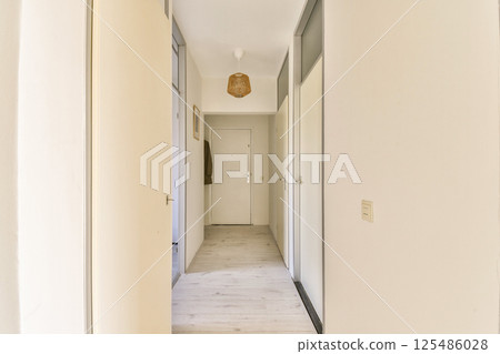 A spacious minimalist hallway featuring light walls, simple design, and a clean wooden floor that enhances the airy atmosphere. 125486028