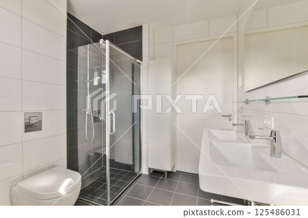 Stylish modern bathroom featuring a sleek glass shower, contemporary sinks, and minimalist decor. The design emphasizes cleanliness and functionality. 125486031
