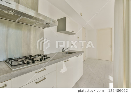 A sleek, contemporary kitchen showcasing minimalist design with white cabinetry, stainless steel appliances, and abundant natural light. 125486032