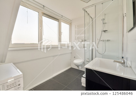 A sleek modern bathroom design featuring a glass shower, toilet, and washing machine, accentuated by ample natural light from large windows. A sleek modern bathroom design featuring a glass shower, toilet, and washing machine, accentuated by ample natural light from large windows. 125486046