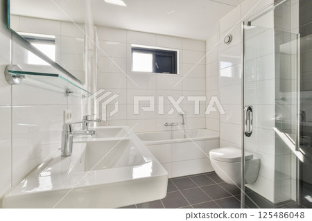 A spacious, bright bathroom featuring sleek white tiles, a contemporary bathtub, and glass shower. Ideal for showcasing modern interior aesthetics. 125486048