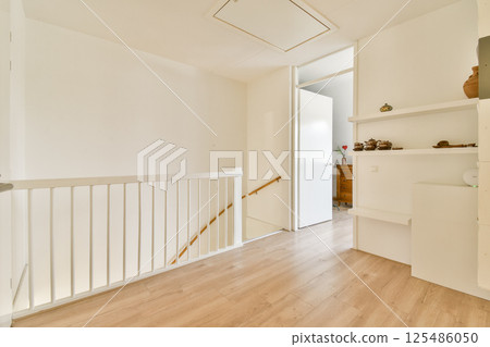 A spacious and well-lit interior hallway featuring wooden flooring, white walls, and an open door leading to another room, creating an inviting atmosphere. 125486050