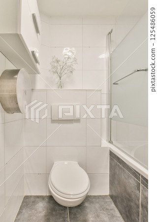 A sleek, minimalist bathroom featuring clean lines, white tiles, and modern fixtures. The space includes a toilet, a glass shower, and a stylish atmosphere. A sleek, minimalist bathroom featuring clean lines, white tiles, and modern fixtures. The space includes a toilet, a glass shower, and a stylish atmosphere. 125486059