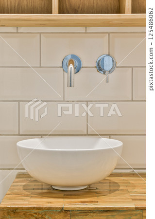 A sleek white bowl sink set against white tiled walls, featuring minimalistic fixtures that enhance the modern aesthetic of the bathroom. A sleek white bowl sink set against white tiled walls, featuring minimalistic fixtures that enhance the modern aesthetic of the bathroom. 125486062