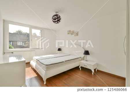 Bright and airy modern bedroom featuring a minimalist design with a white bed, wooden flooring, and a window allowing natural light to illuminate the space. Bright and airy modern bedroom featuring a minimalist design with a white bed, wooden flooring, and a window allowing natural light to illuminate the space. 125486066
