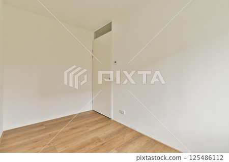 A spacious interior featuring white walls and a wooden floor, radiating a minimalist aesthetic suitable for modern living spaces. 125486112