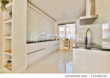 Sleek and minimalistic kitchen design featuring white cabinetry, spacious layout, and natural light streaming through large windows, creating a bright atmosphere. 125486182