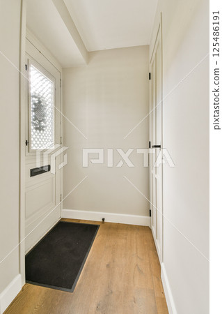 An inviting modern entrance hallway featuring a light-colored design, wooden flooring, and a sleek front door. The minimalist style enhances the spacious feel. An inviting modern entrance hallway featuring a light-colored design, wooden flooring, and a sleek front door. The minimalist style enhances the spacious feel. 125486191