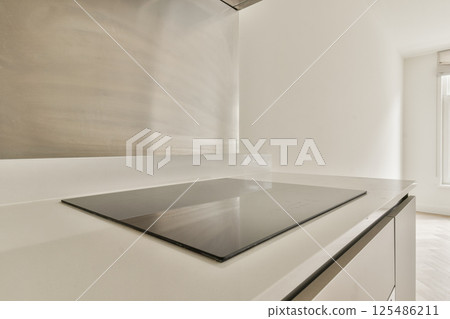 A contemporary kitchen featuring a minimalist design, polished surfaces, and a sleek induction cooktop, emphasizing simplicity and functionality. 125486211