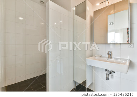 This image showcases a sleek and contemporary bathroom with elegant white tiles and a stylish sink, enhancing its spacious feel and cleanliness. 125486215