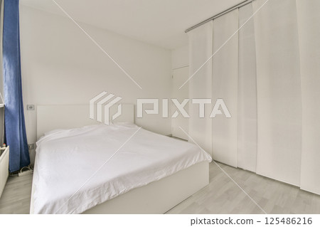 A clean and minimalistic bedroom showcasing a white bed and simple decor against a light background, promoting a serene atmosphere. 125486216