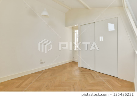 A spacious, minimalist room featuring wooden flooring and white walls. Natural light streams through the large window, enhancing the serene atmosphere. 125486231