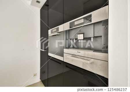 Sleek, contemporary kitchen featuring dark cabinets and minimalist design with a mirrored finish, optimizing space and aesthetics. Sleek, contemporary kitchen featuring dark cabinets and minimalist design with a mirrored finish, optimizing space and aesthetics. 125486237
