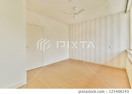 Bright, minimalist room featuring a light wooden floor, neutral walls with subtle stripes, and natural light streaming through the window. 125486243