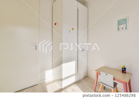 A well-lit minimalist child's room featuring a white wardrobe and a small desk, ideal for creating a cozy and organized space for kids. A well-lit minimalist child's room featuring a white wardrobe and a small desk, ideal for creating a cozy and organized space for kids. 125486298
