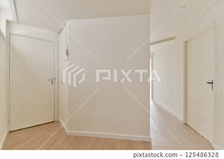 A serene and minimalist interior hallway featuring clean lines and neutral colors. The light wood flooring complements the bright walls. 125486328