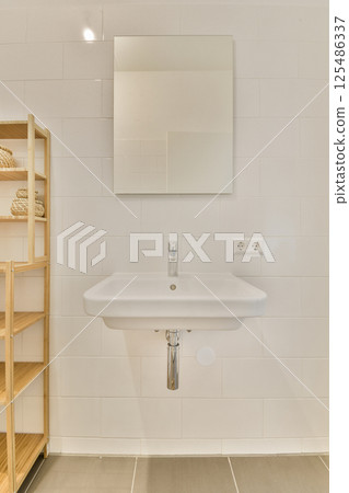 A sleek and contemporary bathroom featuring a minimalist sink, a wall-mounted mirror, and wooden shelving, creating a functional yet stylish space. 125486337