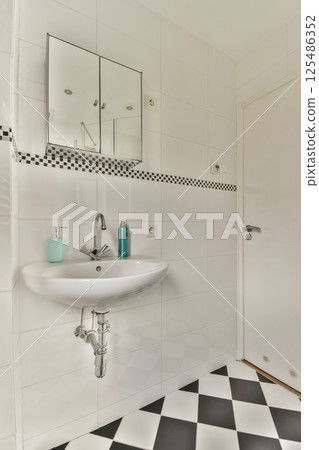 A stylish bathroom featuring a sleek white sink, a large mirror, and striking black and white checkered flooring, showcasing contemporary design elements. 125486352