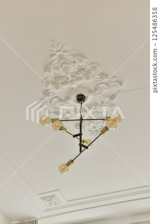 A stylish modern chandelier featuring multiple bulbs, suspended from a textured ceiling that showcases an intricate design, blending sophistication with contemporary aesthetics. A stylish modern chandelier featuring multiple bulbs, suspended from a textured ceiling that showcases an intricate design, blending sophistication with contemporary aesthetics. 125486358