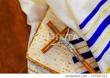 Crucifix on matzo bread, draped in tallit prayer shawl ceremonial cloth, symbolizes religious meaning at festivity. 125487222