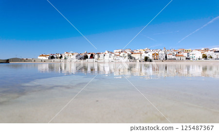 A picturesque coastal town with whitewashed buildings reflects on the calm waters of a lagoon A picturesque coastal town with whitewashed buildings reflects on the calm waters of a lagoon 125487367