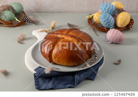 A delicious folar cake is presented with two nests of decorated Easter eggs and soft feathers 125487489