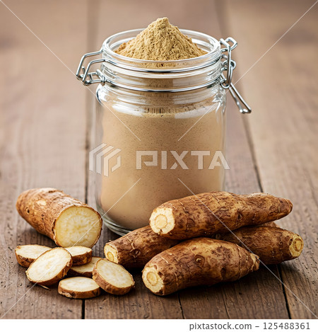 A glass jar filled with yacon powder sits on a wooden surface, surrounded by whole and sliced yacon roots 125488361