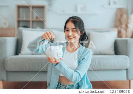 Young Asian woman holding piggy bank and sitting on the floor at home 125489058