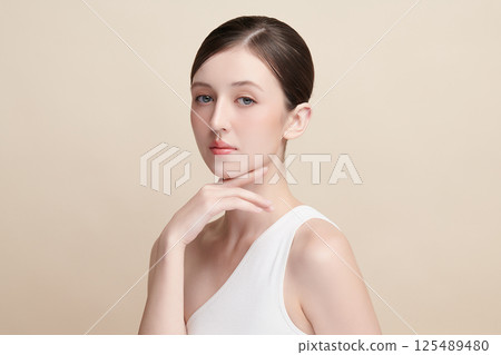 A beautiful young woman with clean, fresh skin against a beige background. Skincare, facial treatment, cosmetology, beauty, and spa. An elegant portrait of an woman. 125489480