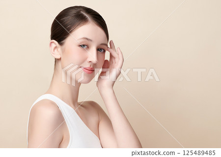 A beautiful young woman with clean, fresh skin against a beige background. Skincare, facial treatment, cosmetology, beauty, and spa. An elegant portrait of an woman. 125489485