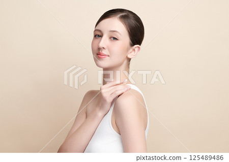 A beautiful young woman with clean, fresh skin against a beige background. Skincare, facial treatment, cosmetology, beauty, and spa. An elegant portrait of an woman. 125489486
